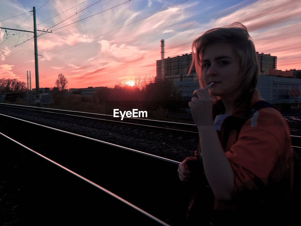 Portrait of young woman standing on railroad track during sunset