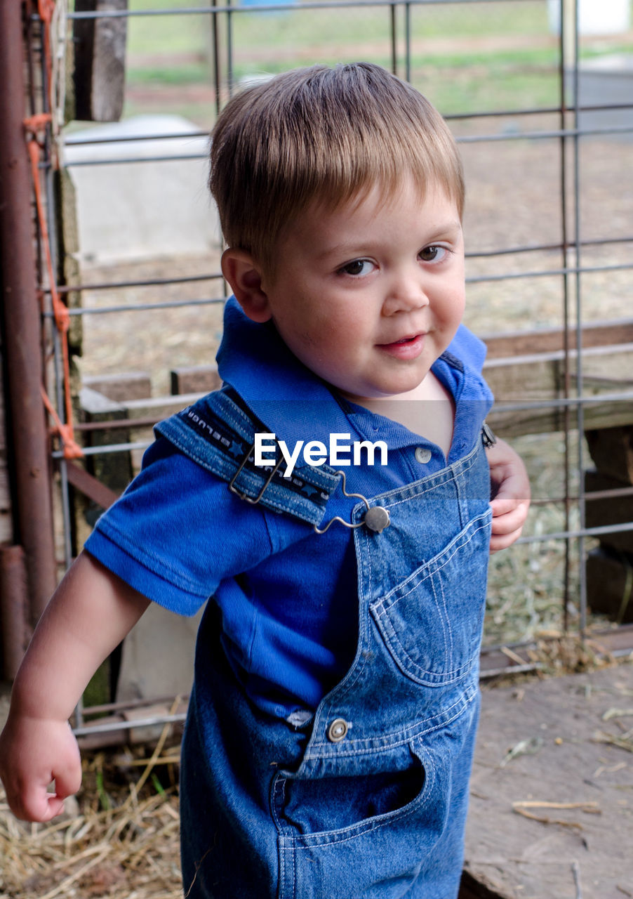 Toddler in overalls smiles as he walks around the farm yard