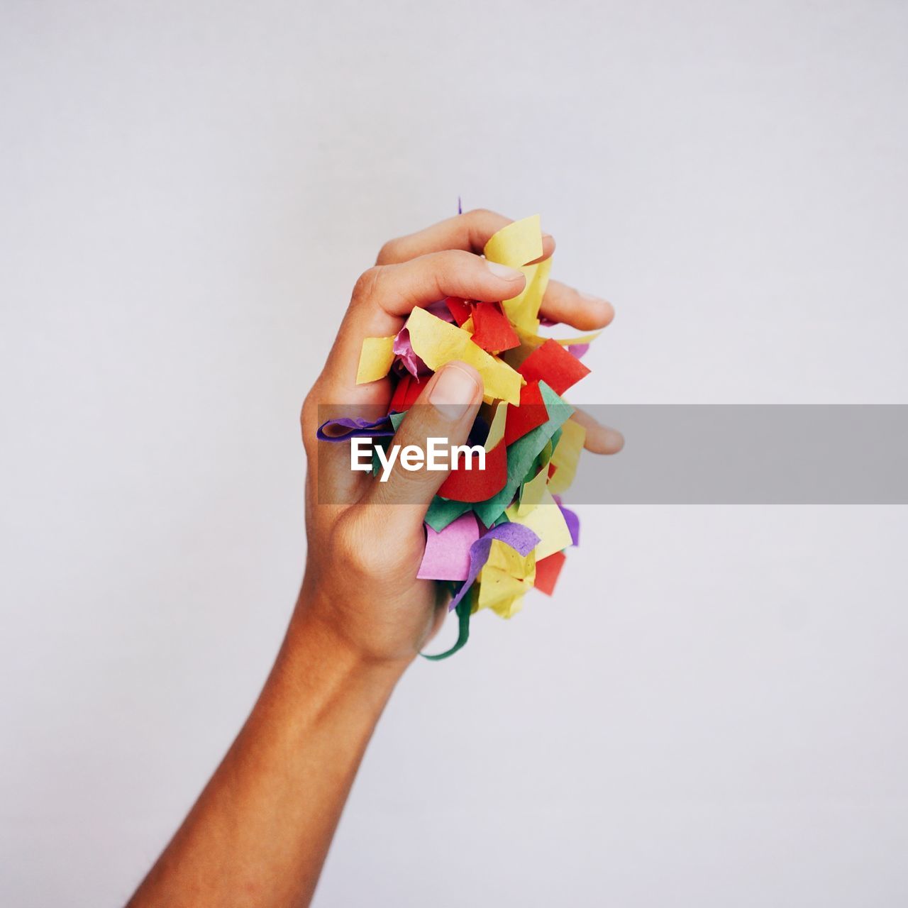 Cropped image of hand holding confetti against white background