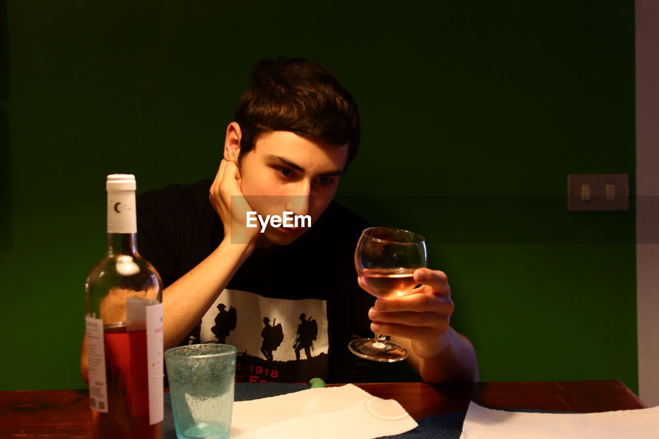 A puzzled caucasian boy reflects looking at a glass of wine