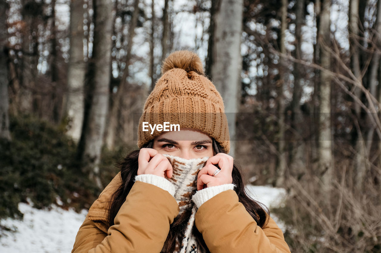 Portrait of young woman holding scarf over her face. winter, outdoors, warm clothes.