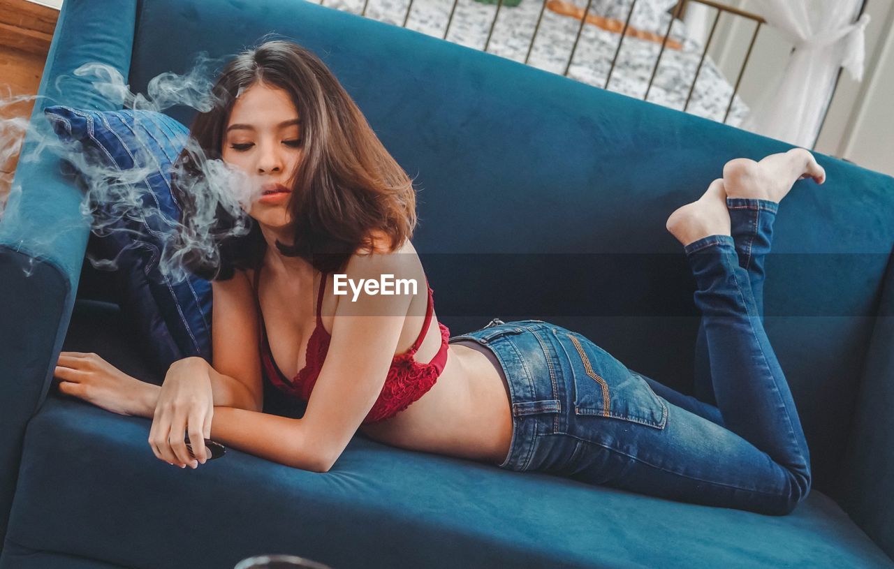 Young woman smoking electronic cigarette while lying on sofa