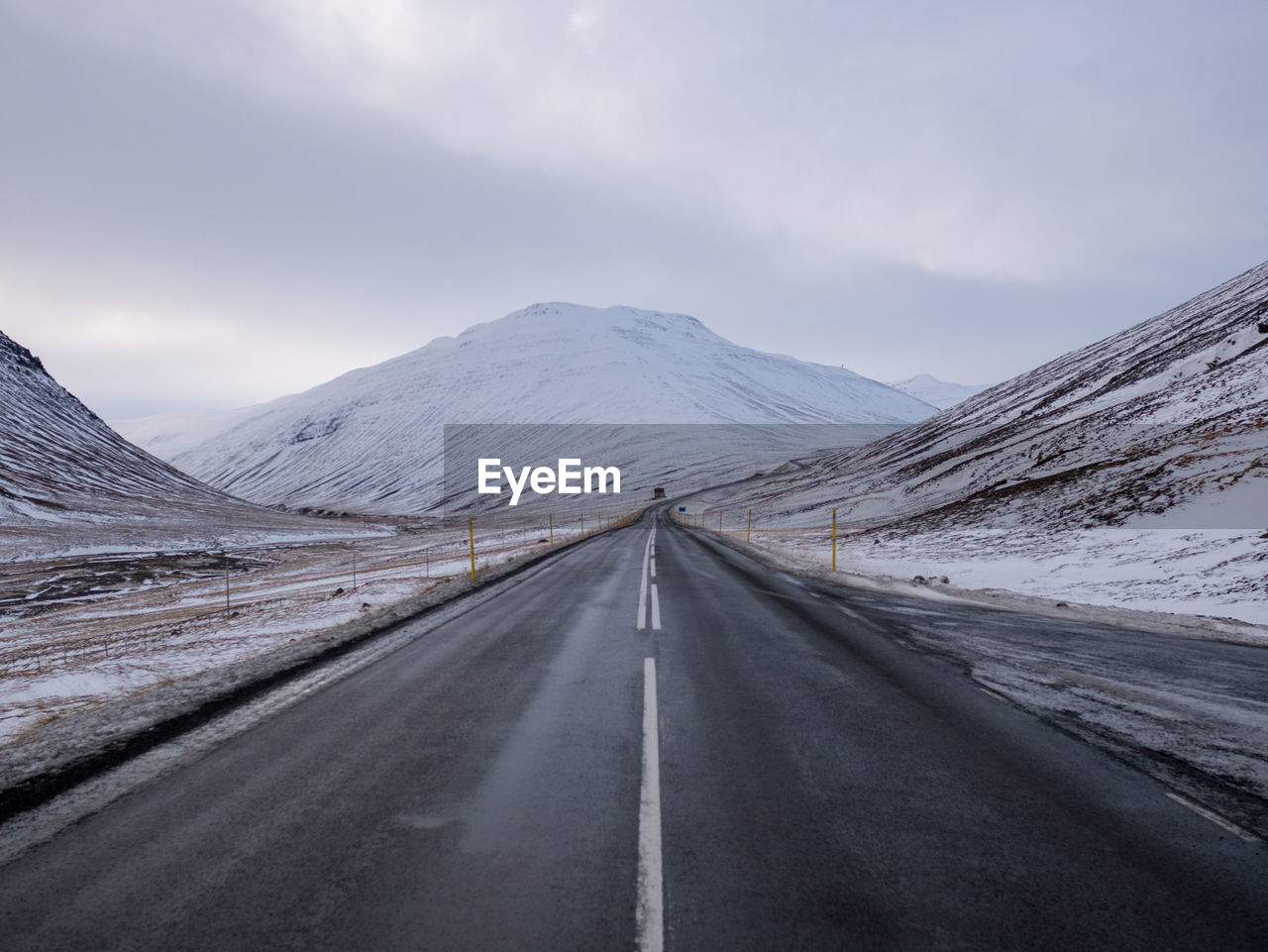 Empty road amidst snow covered mountains against sky