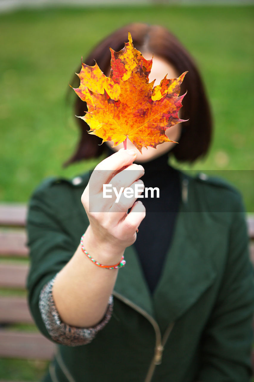 CLOSE-UP OF WOMAN HOLDING AUTUMN LEAVES