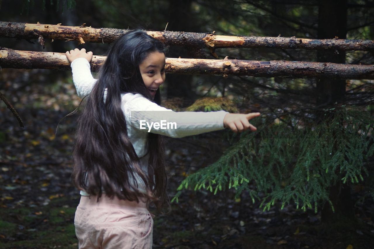 Rear view of girl with long hair gesturing while standing in forest