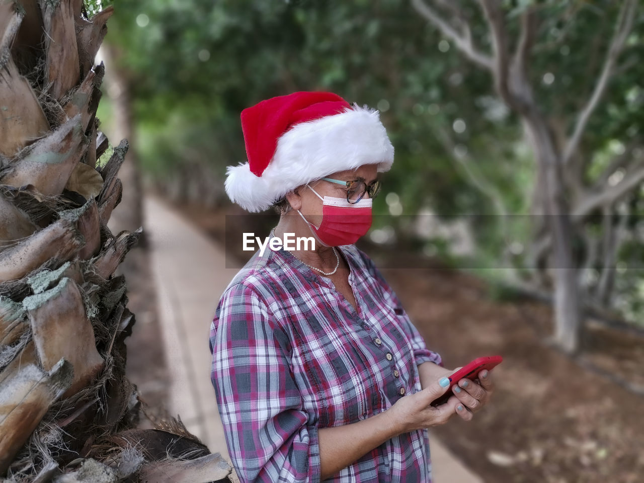 Senior woman wearing mask using smart phone while standing outdoors