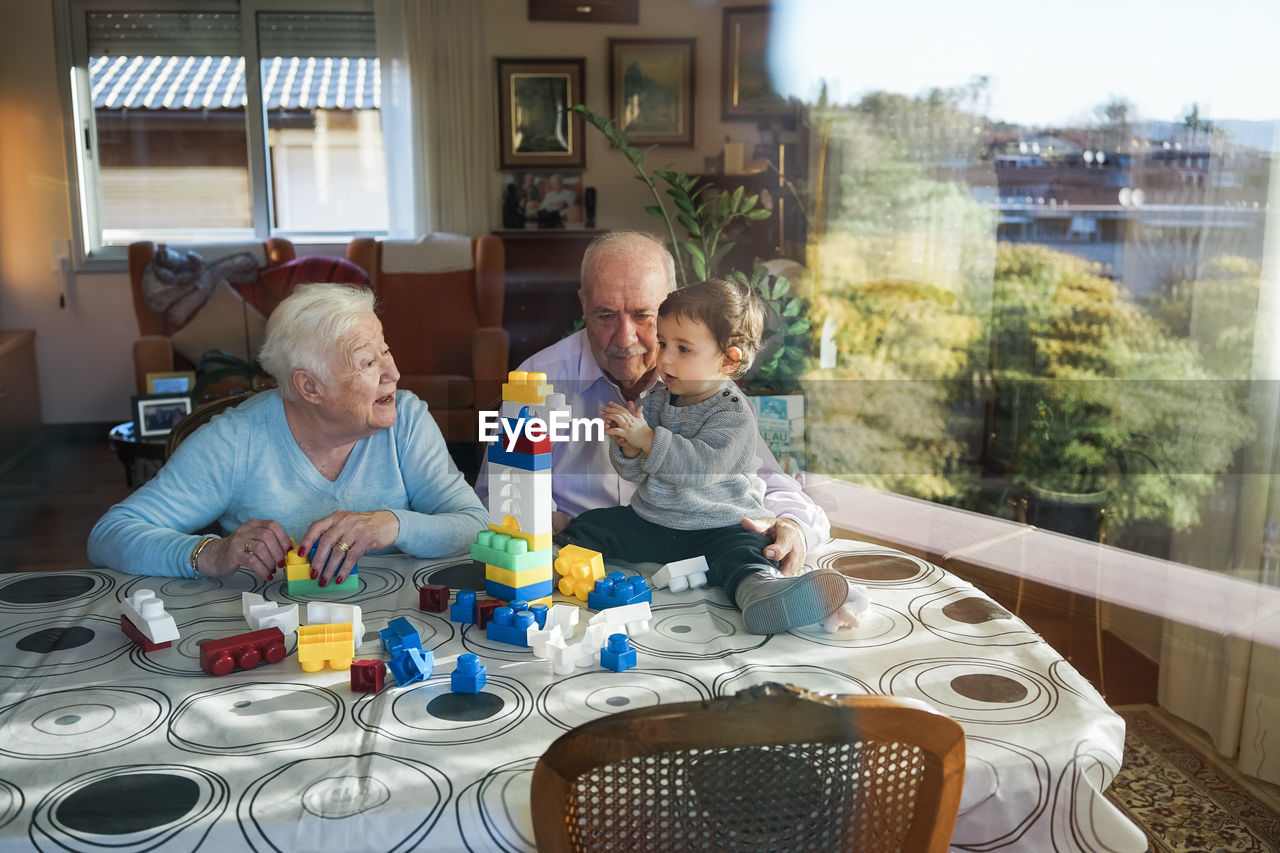 Great-grandparents and baby girl playing together with plastic building bricks at home