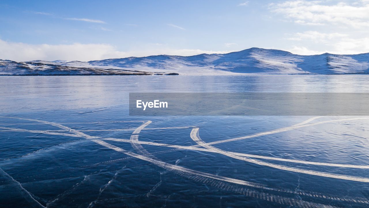 Frozen lake and mountains against sky during sunny day