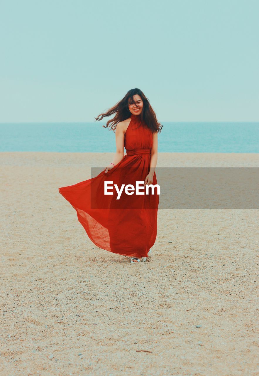 Smiling woman standing on beach against sky