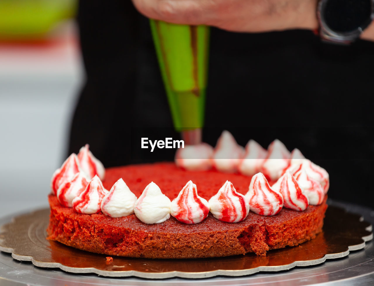 Baker cooking red velvet cake, putting cream icing.