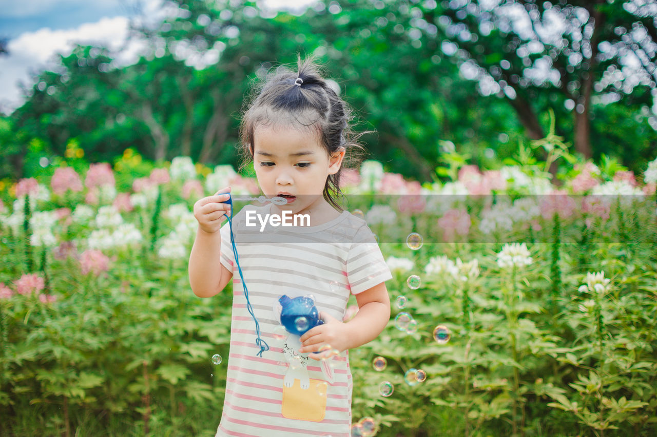 Girl holding bubble wand against flowers at park