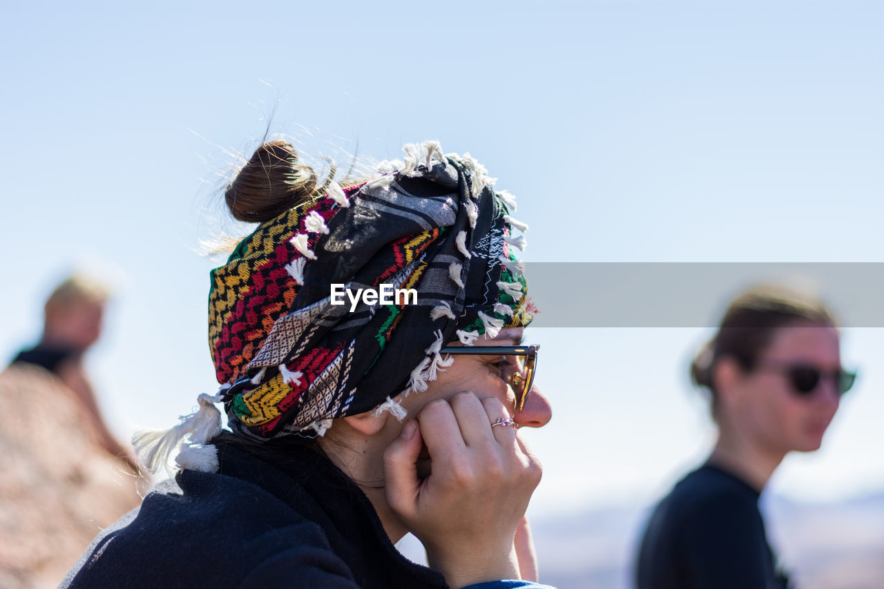 Side view of woman with hands on cheek against sky