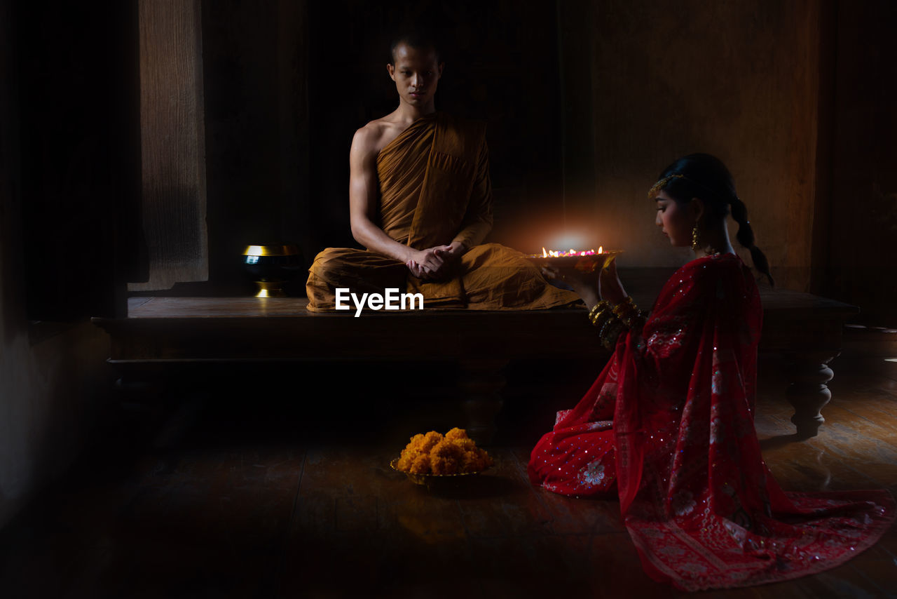 Side view of woman giving religious offering to monk in temple