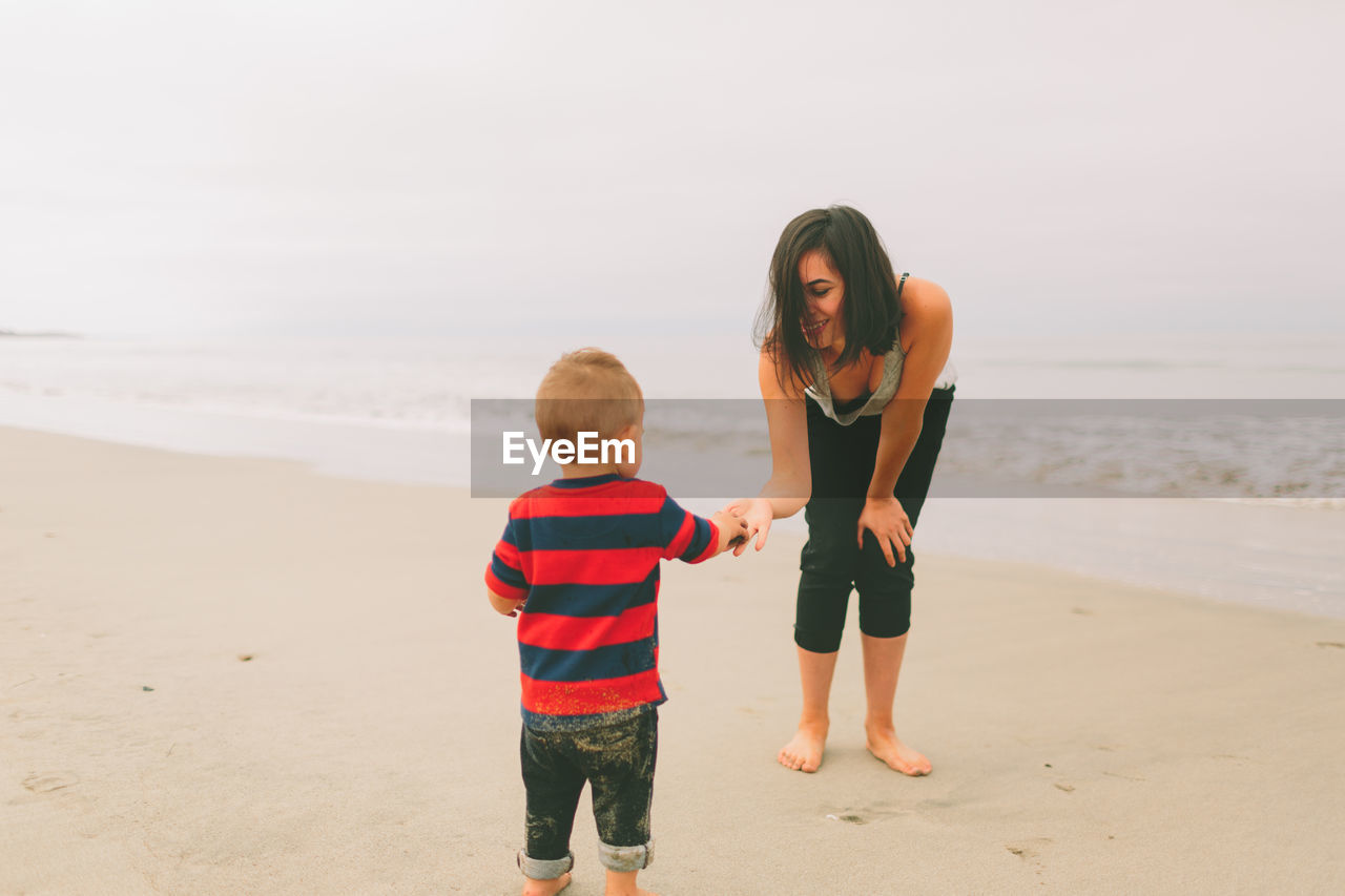 Mother and son standing at beach against sky