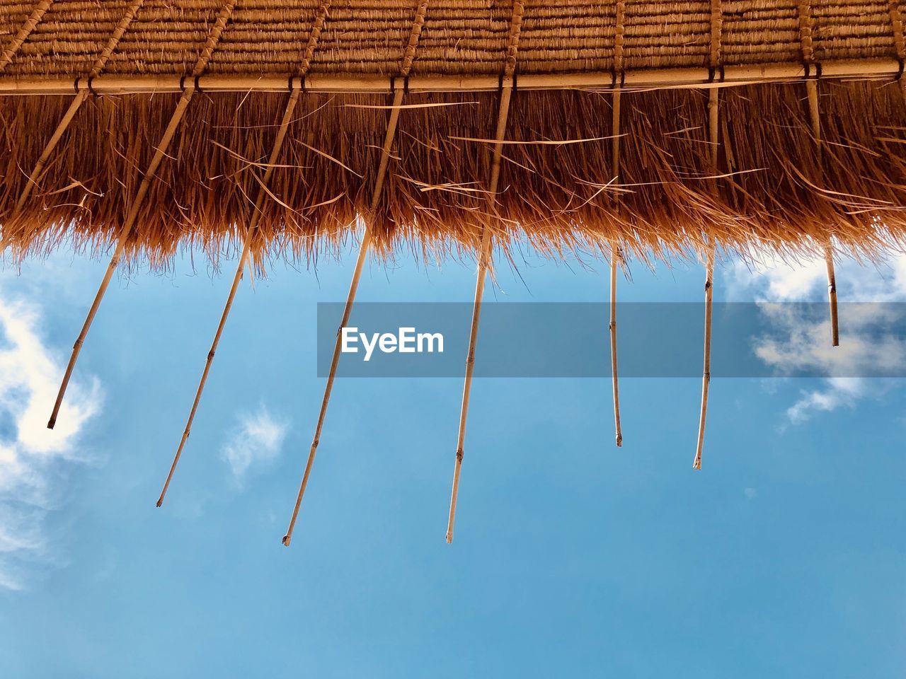 Directly below shot of thatched roof parasol against blue sky