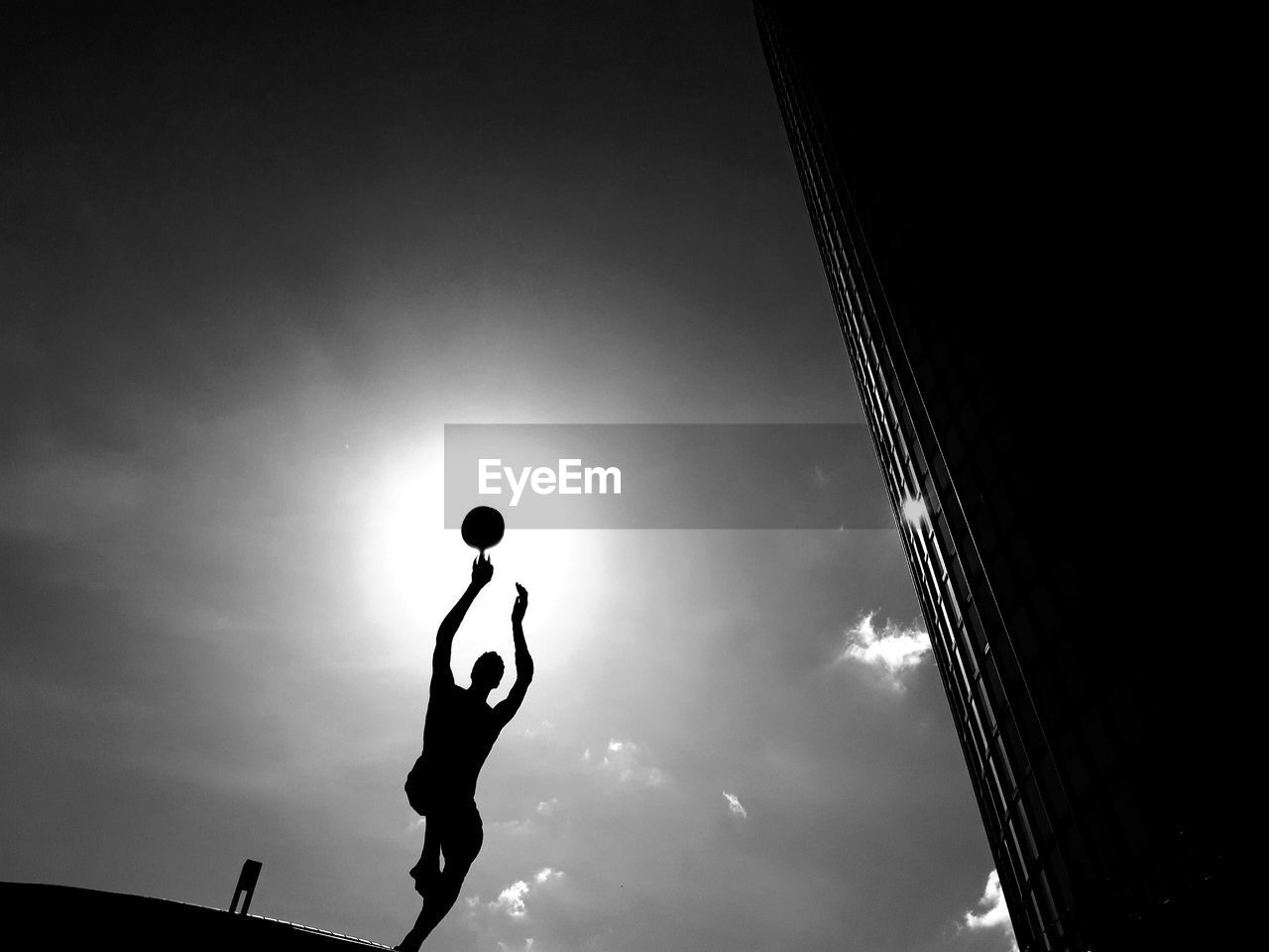 Low angle view of silhouette man playing with ball against sky