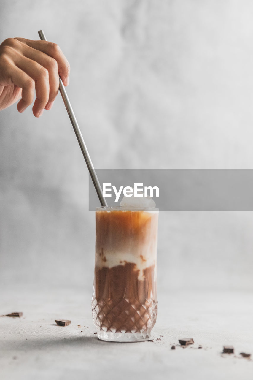 Midsection of person holding metal straw in iced coffee drink on table