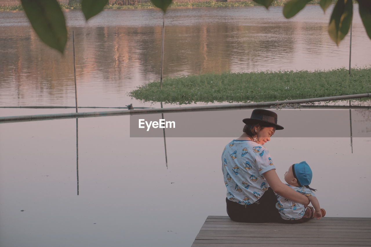 Rear view of mother with baby sitting on pier over lake