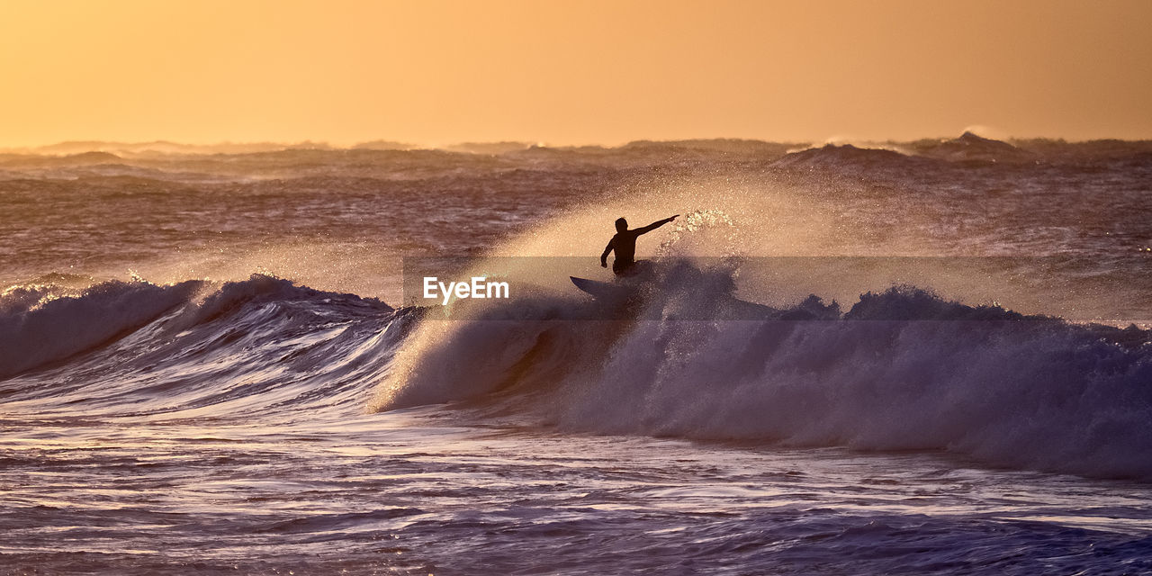 Silhouette man surfing in sea against sky