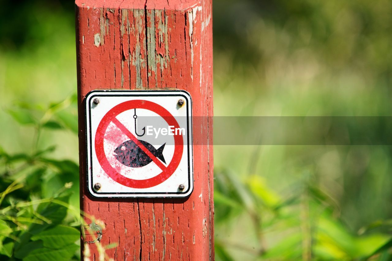 Close-up of warning sign on wooden post