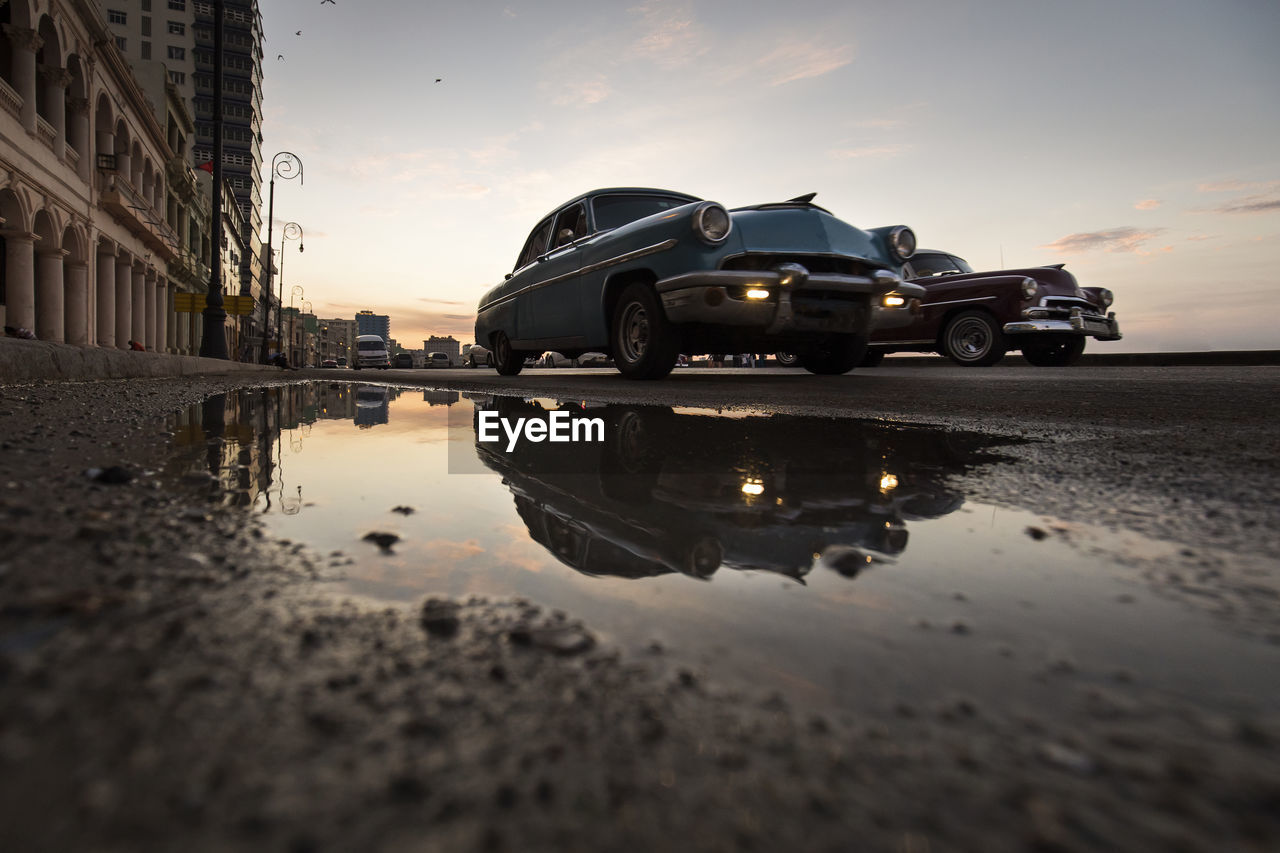 REFLECTION OF BUILDING IN PUDDLE ON ROAD IN CITY