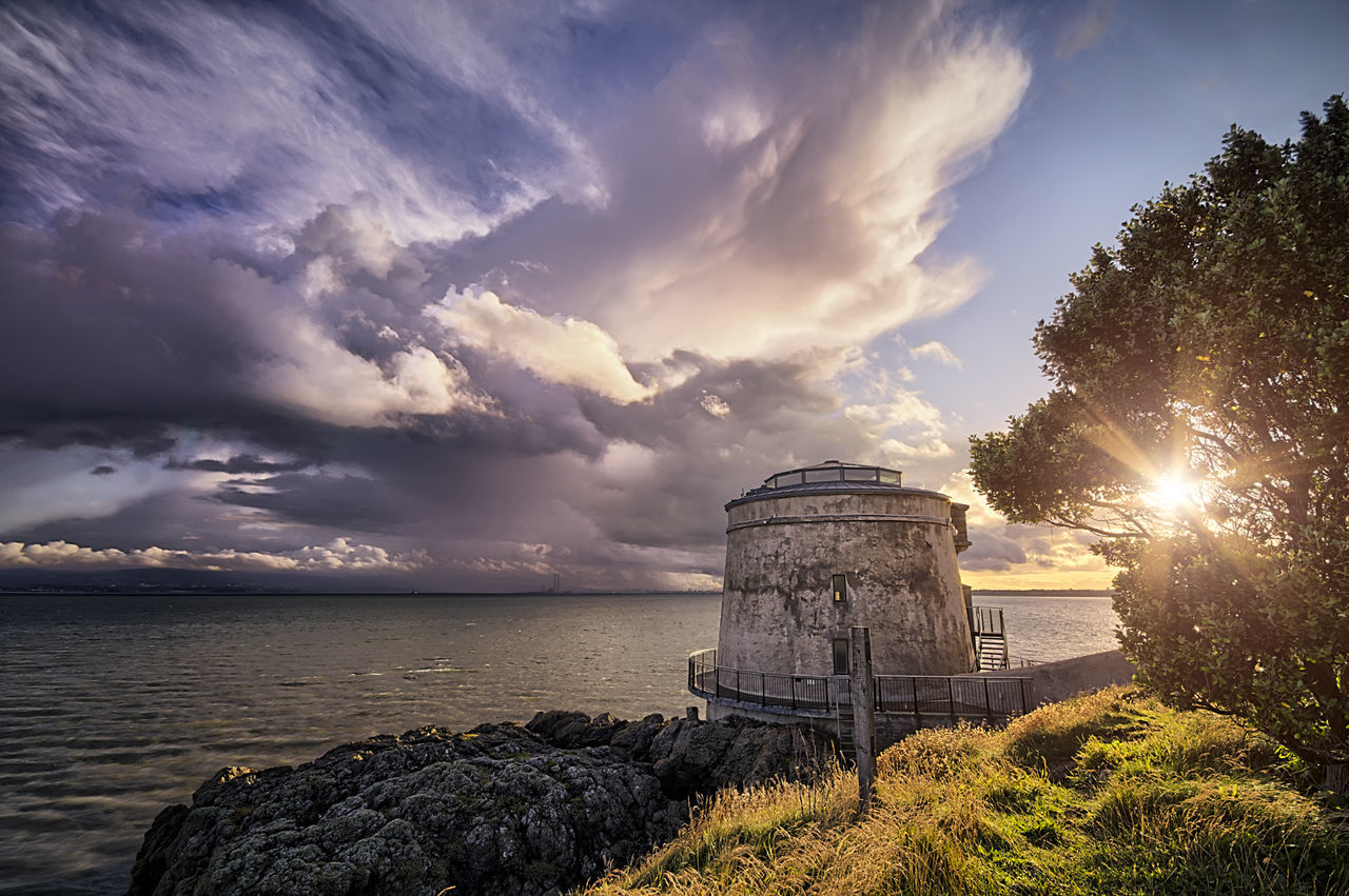 Built structure by river against sky at sunset