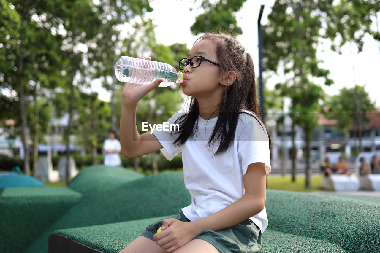 Girl drinking water while sitting on seat in park