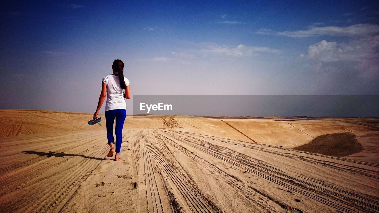 Rear view of woman walking on sand against blue sky at desert