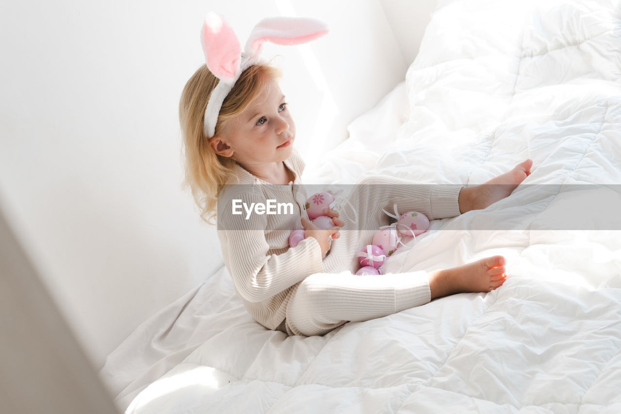 Kid, girl wearing bunny ears playing with colourful eggs on bed.concept of spring and easter holiday