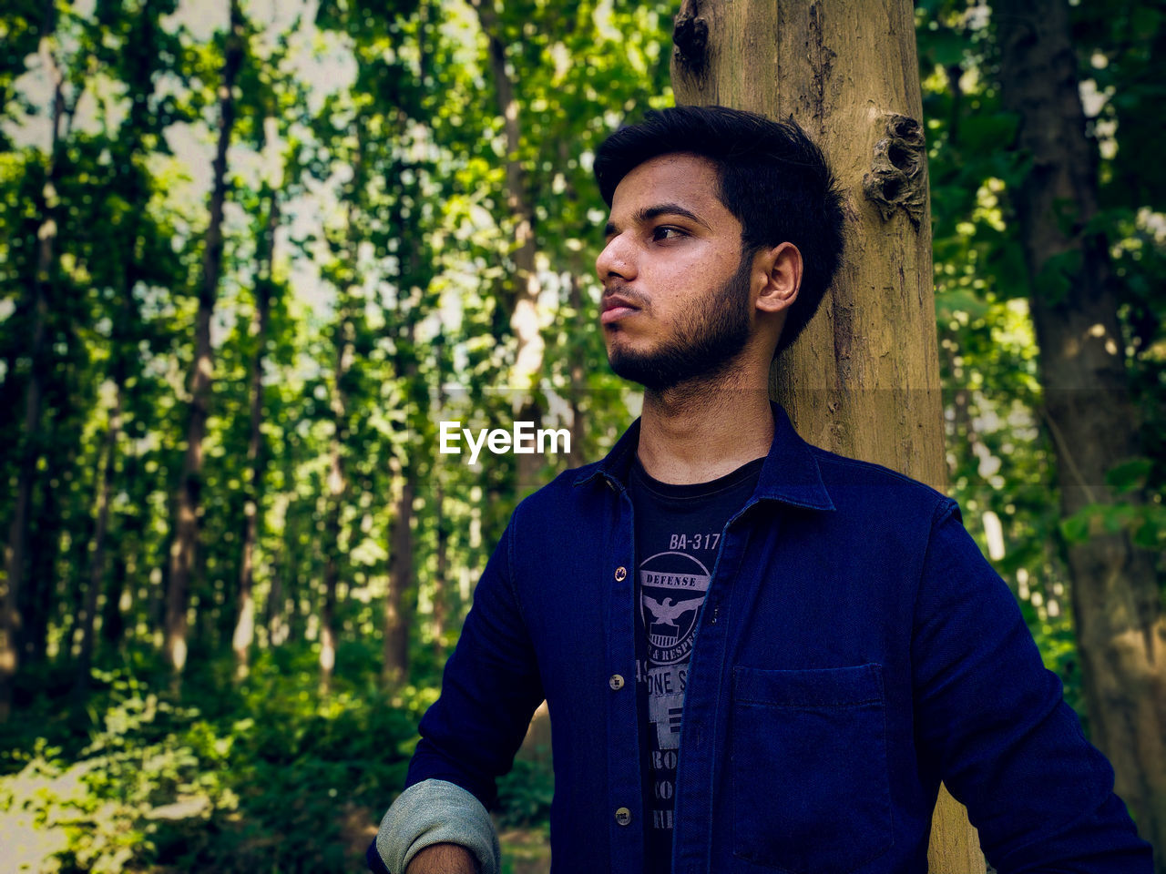 Young man looking away while standing in forest