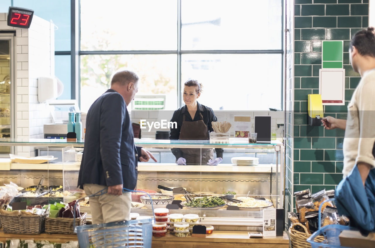 Mature man buying groceries from saleswoman in supermarket