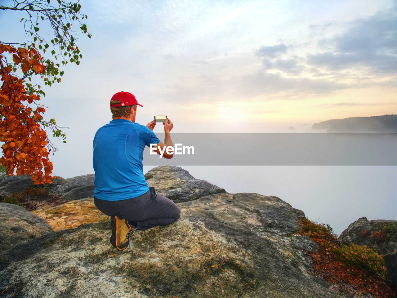 Hiker takes selfie photo, fall nature adventure. man sit on stone on mountain sumit daybreak horizon