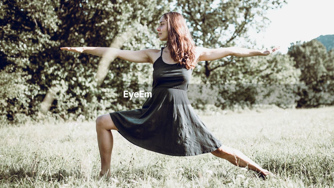 Beautiful young woman exercising on grassy field during sunny day