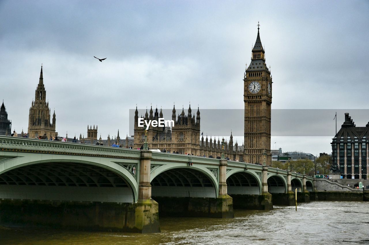 Westminster bridge over thames river by big ben against cloudy sky