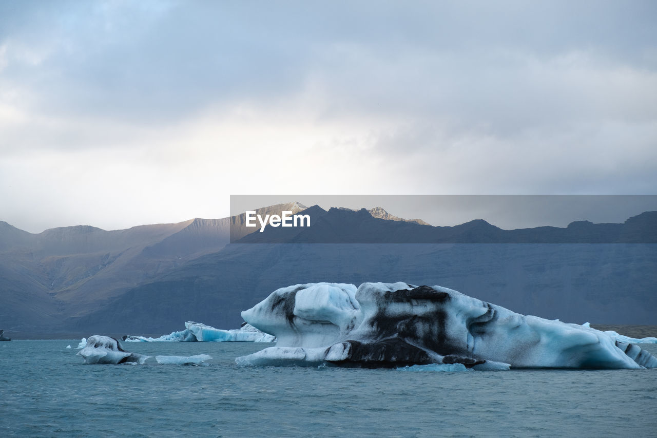 Scenic view of iceberg, sea and mountains against sky in the southern coast of iceland 