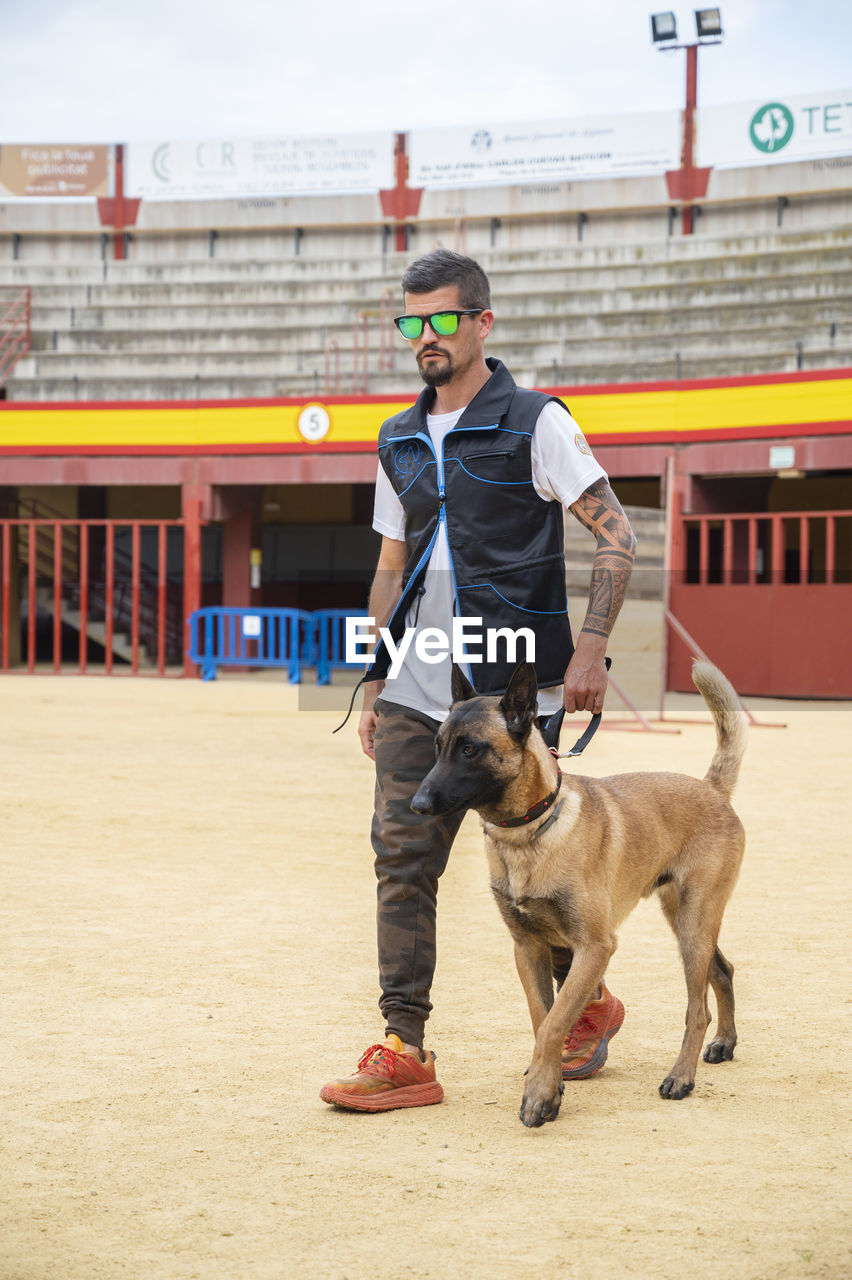 domestic animals, animal themes, animal, mammal, one animal, animal sports, dog, pet, full length, one person, men, adult, canine, carnivore, sports, architecture, clothing, young adult, person, standing, day, bullring, lifestyles, leisure activity, motion, livestock