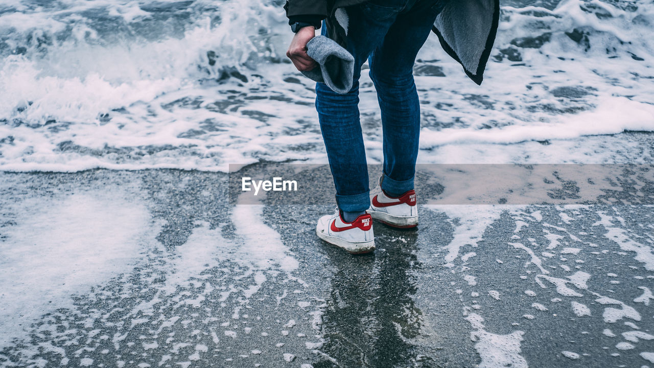 LOW SECTION OF PERSON STANDING ON SNOW COVERED LANDSCAPE