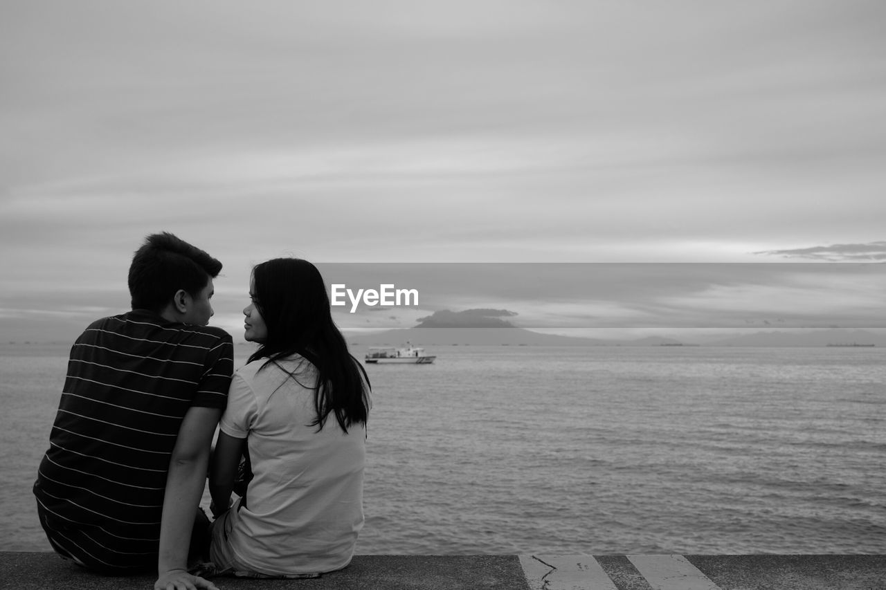 Rear view of couple on beach against sky