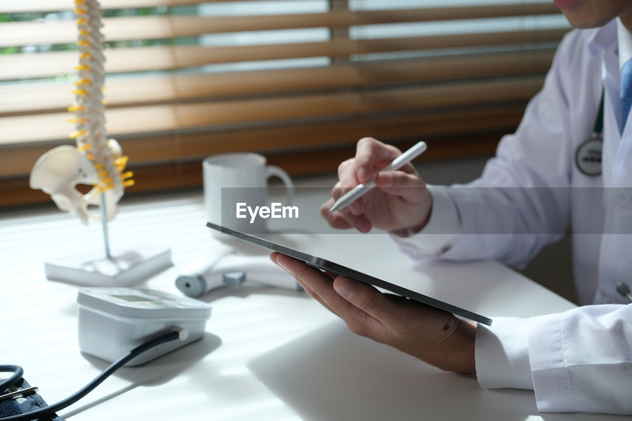 midsection of doctor working at desk in office