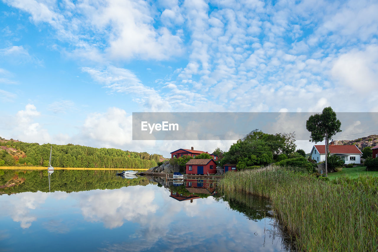 REFLECTION OF HOUSE ON LAKE AND BUILDING AGAINST SKY