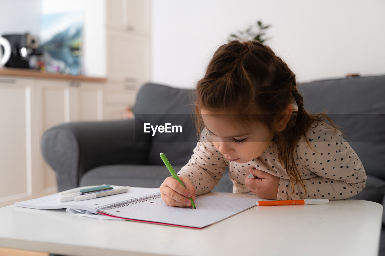 Portrait of cute preschooler child girl drawing with pencils at home while sitting in front 