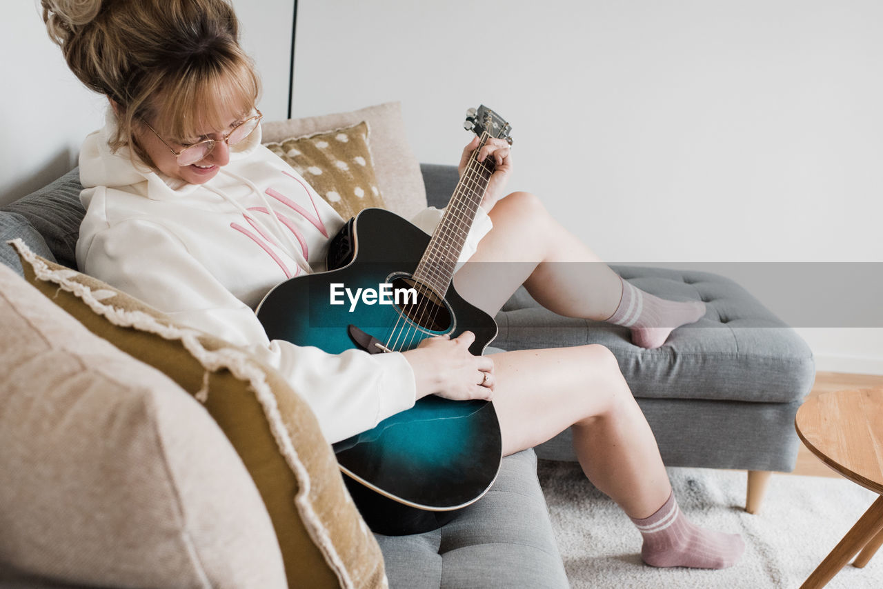 Woman sat playing guitar at home on the couch