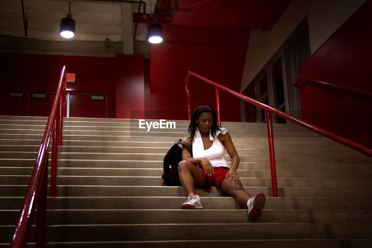 Woman looking leg while sitting on stairs in stadium