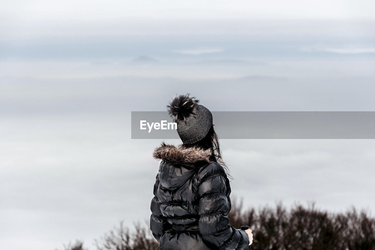 Rear view of woman admiring view from top of hill. winter, fog, hiking, nature.