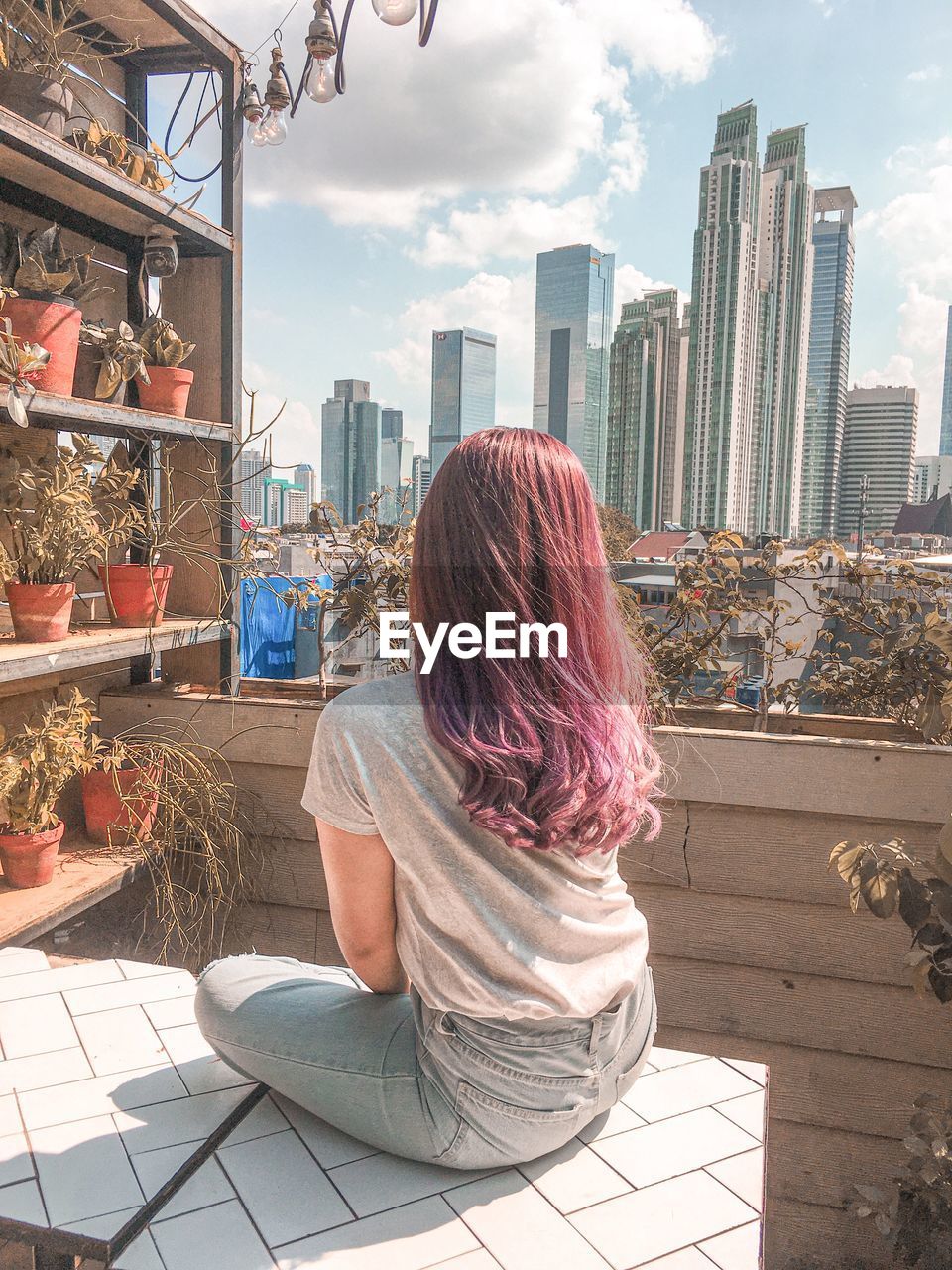 REAR VIEW OF WOMAN SITTING ON BUILDINGS AGAINST SKY