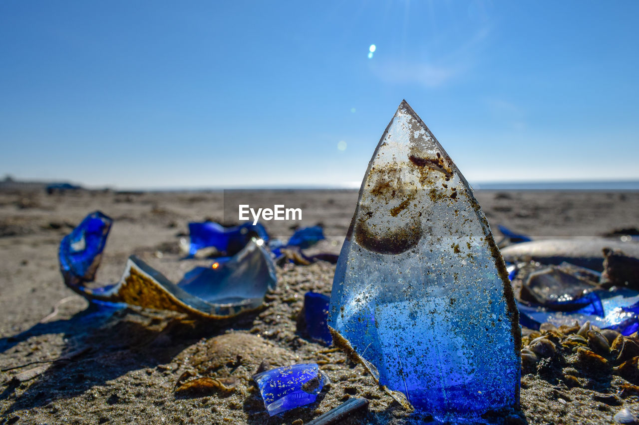 Close-up of broken glass at beach against blue sky