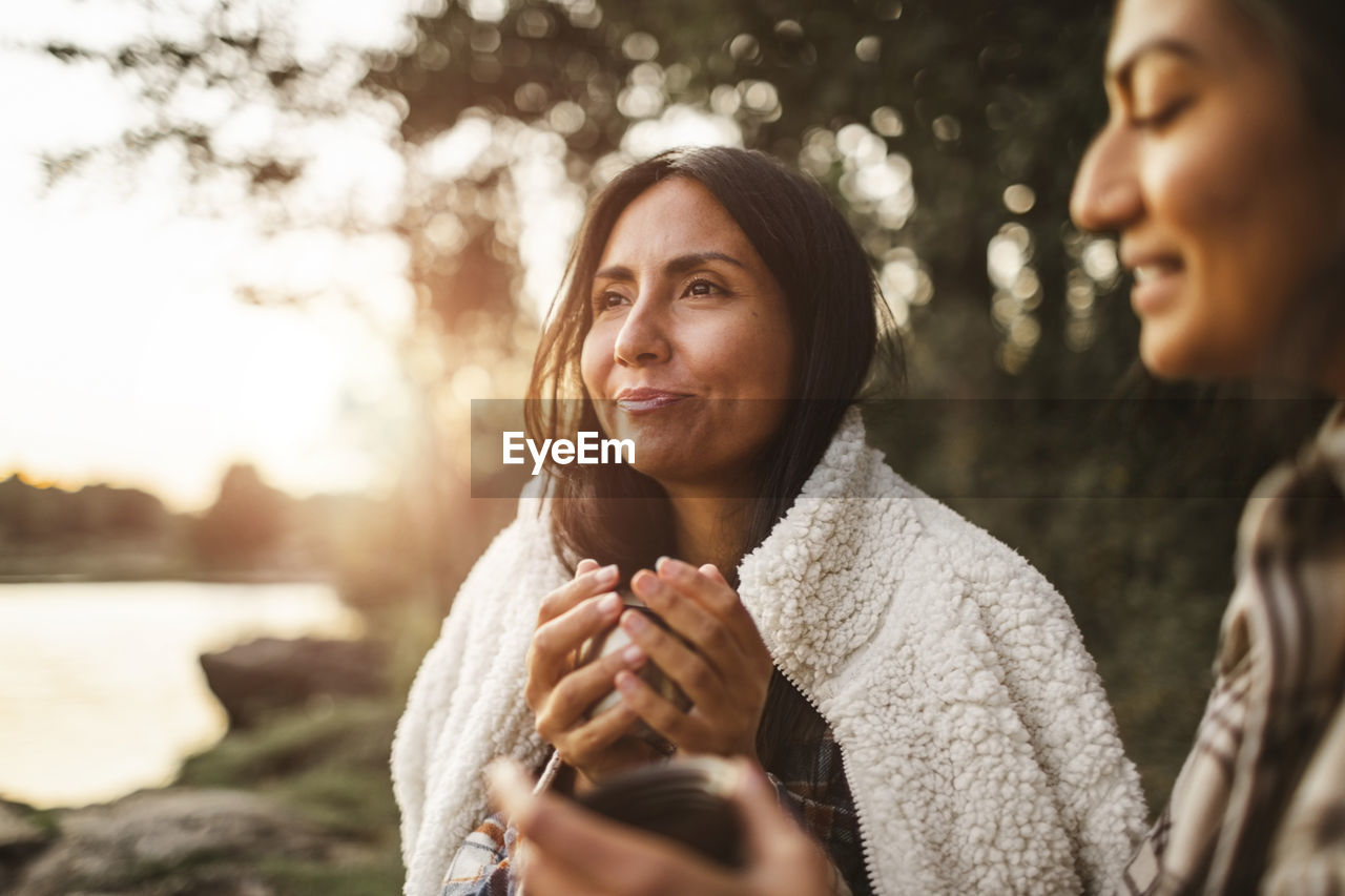 Female friends talking while drinking coffee in forest