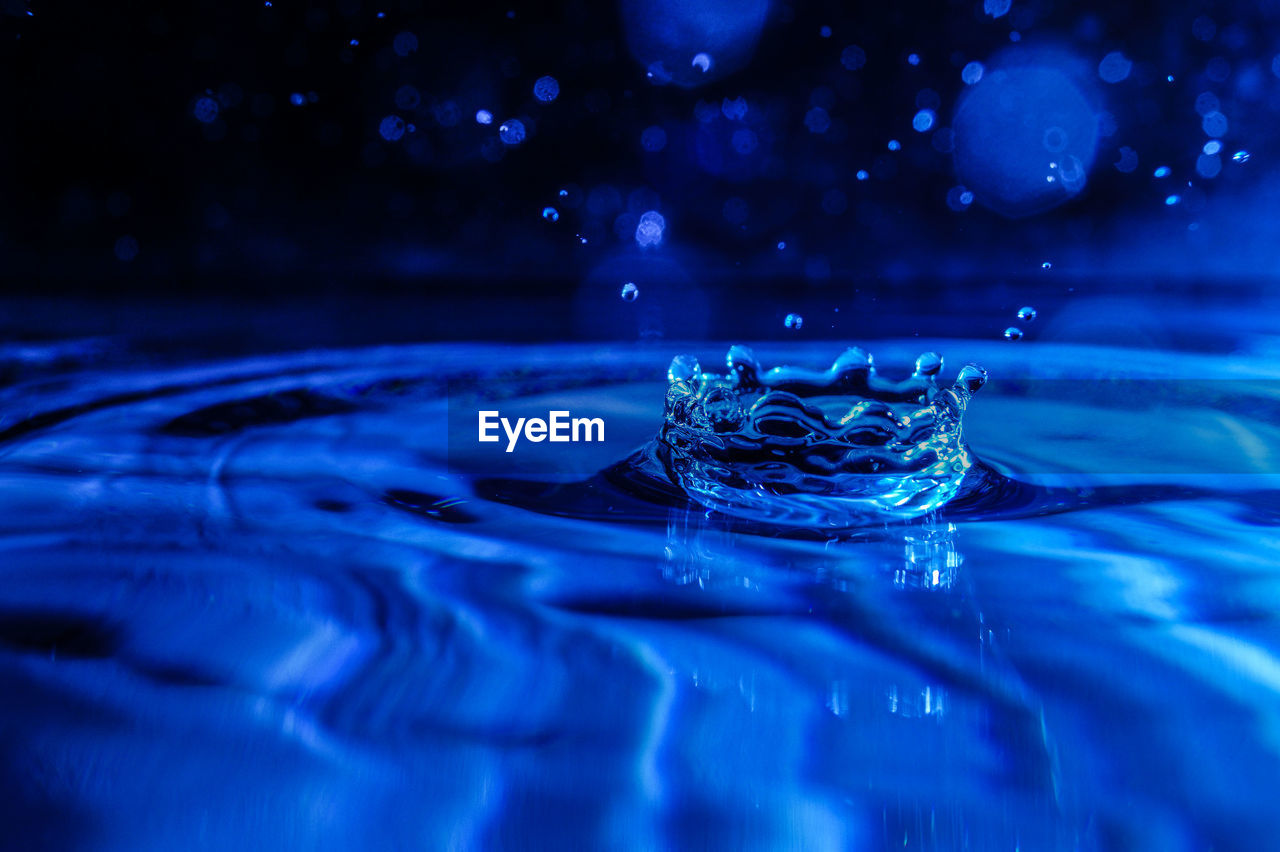 Close-up of splashing droplet in blue water against black background