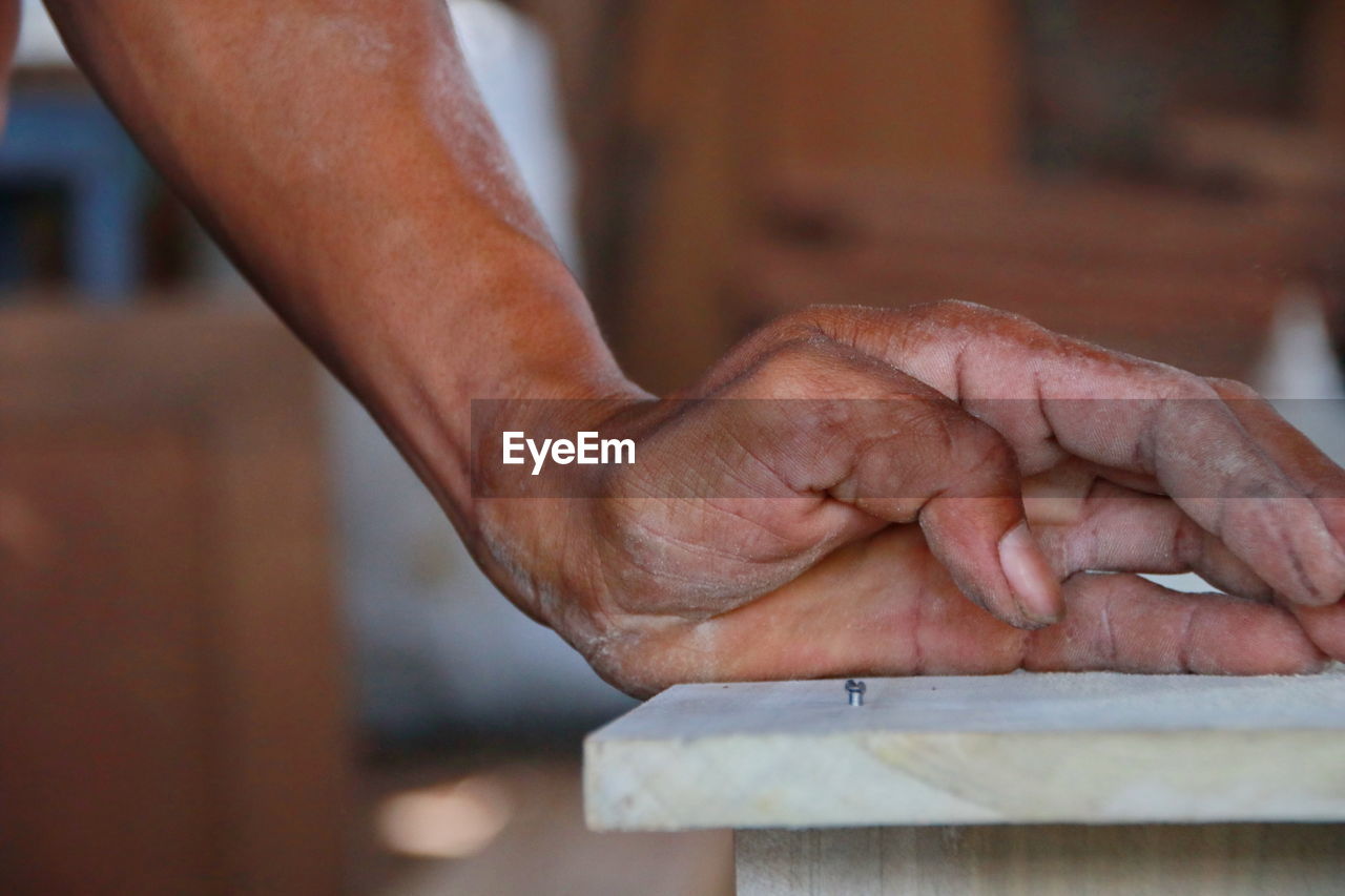 Cropped hand by nail mounted in wooden plank