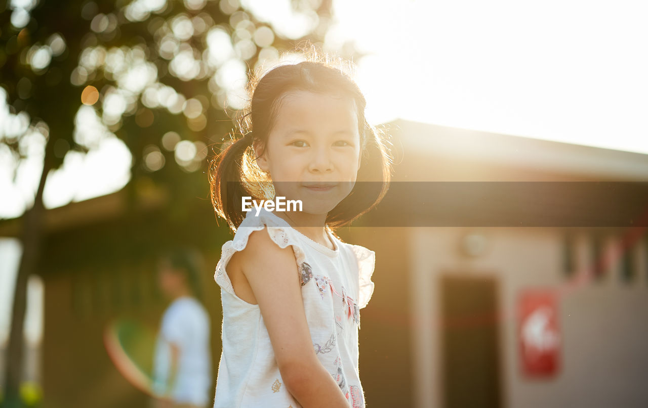 PORTRAIT OF CUTE GIRL STANDING AGAINST BLURRED BACKGROUND
